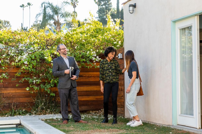 Makler, Vermieterin und Mieterin stehen im grünen Garten mit Pool der Einliegerwohnung nach erfolgreicher Besichtigung.