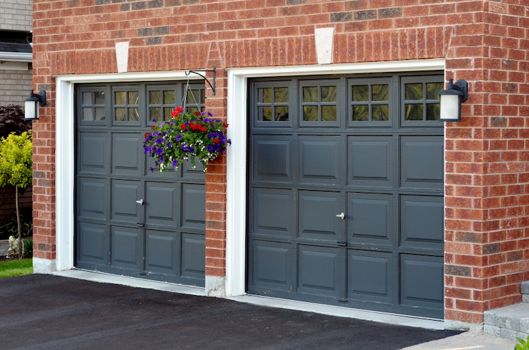 Ein rotes Backsteinhaus mit zwei dunkelgrauen Garagentoren, Blumenkasten und weißem Rand